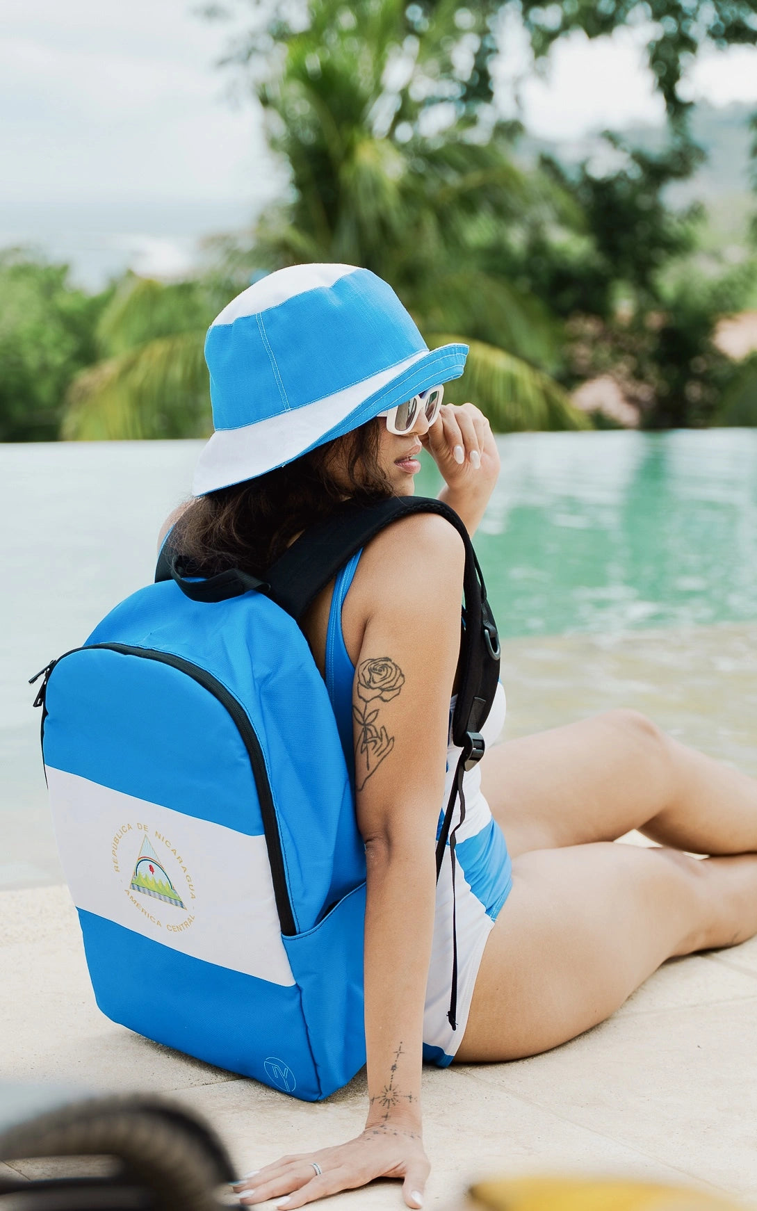 Model wearing Travaly’s Nicaragua flag backpack and matching swimwear by the poolside — vibrant blue design for travel and summer style.
