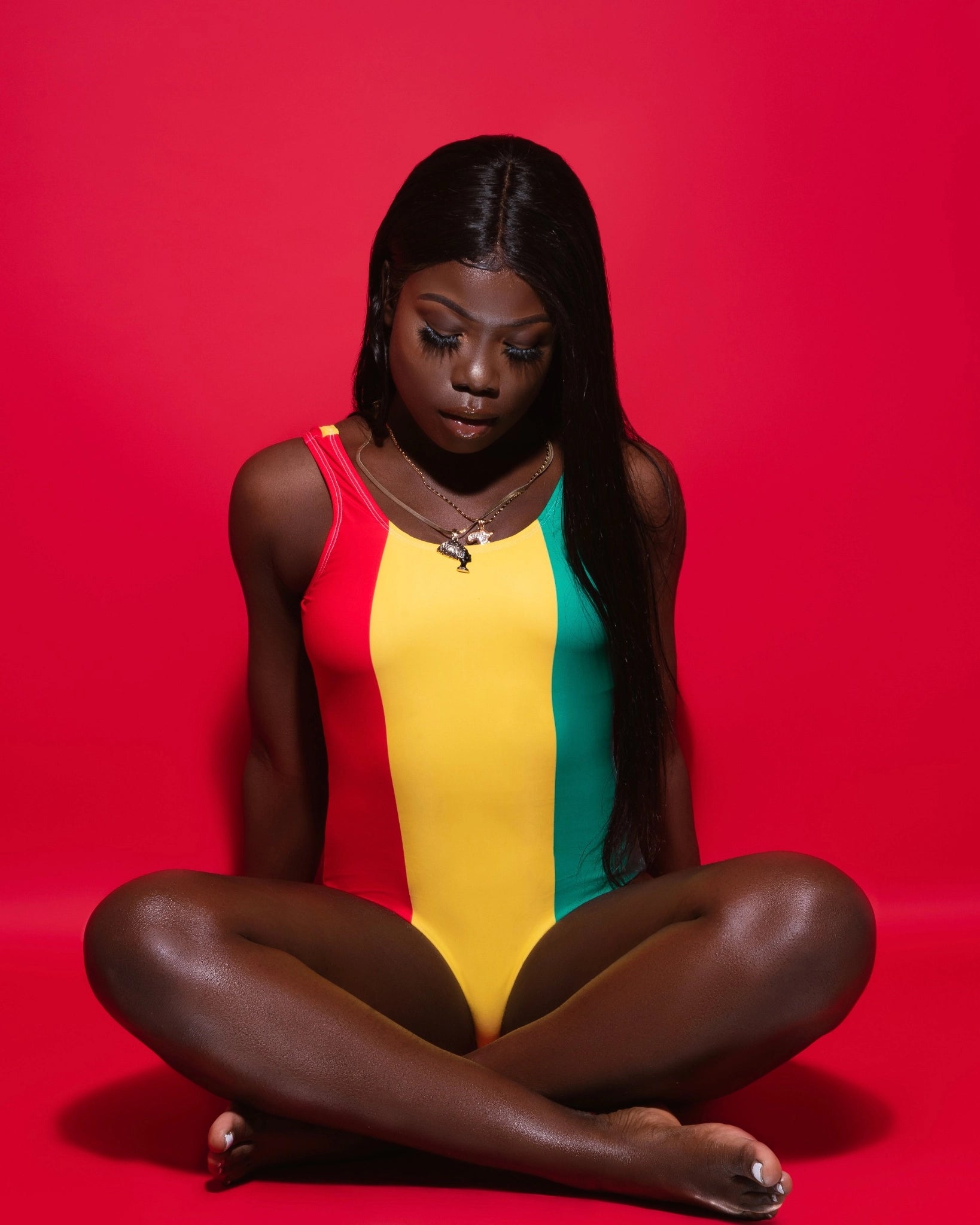 Front view of women's one-piece swimsuit inspired by the Guinea flag, photographed against a red backdrop.